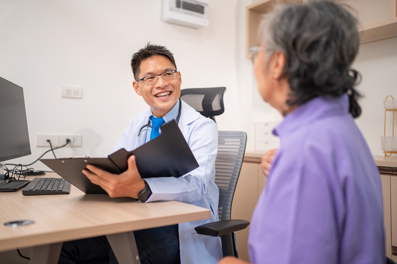 Mature male doctor taking care and talking mature female patient sitting on table in hospital. Medical and Healthcare concept.