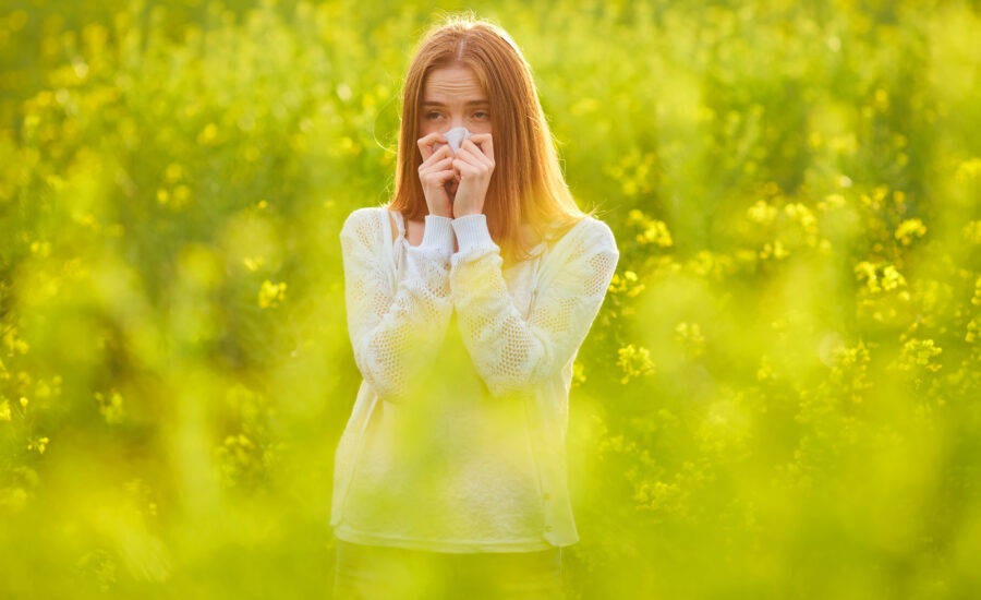 Woman holding a tissue to her nose in a field of yellow flowers during hay fever season