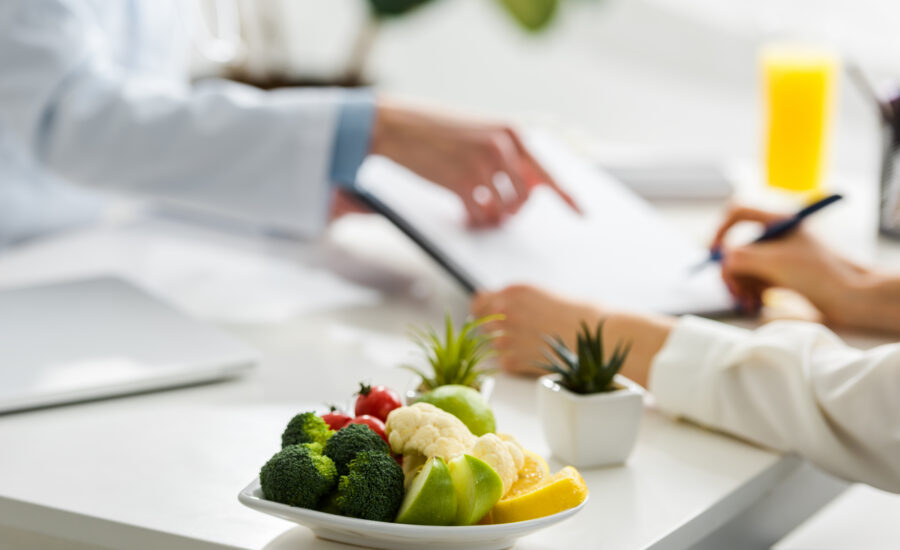Dietitian reviewing a nutrition plan with a patient, with a plate of fresh vegetables and fruit on the desk